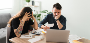 Wife looking down at a calculator and husband looking frustrated over bills and money