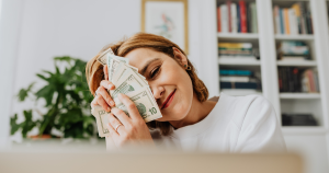 Woman holding dollar bills up to her face and smiling