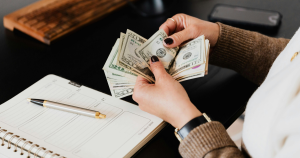 Woman's hands counting twenty dollar bills over an accounting book