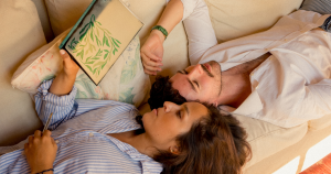 Couple lying on a sofa with the woman reading from a book