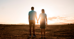 Couple standing on the beach as the sun goes down holding hands