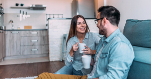 Couple sitting on a couch with coffee mugs smiling and talking